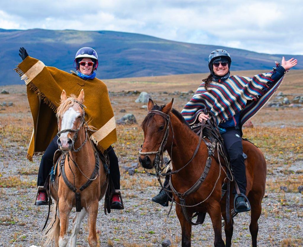 Two riders in traditional ponchos on horseback near Cotopaxi