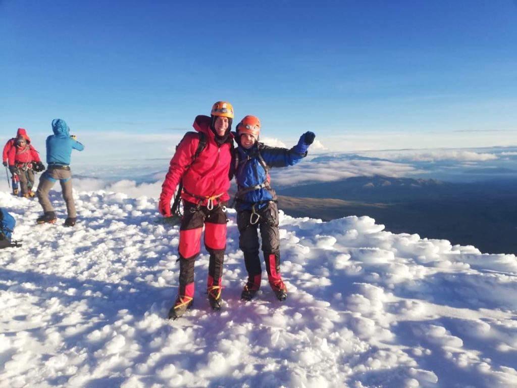 Two climbers celebrating on a snowy summit at sunrise